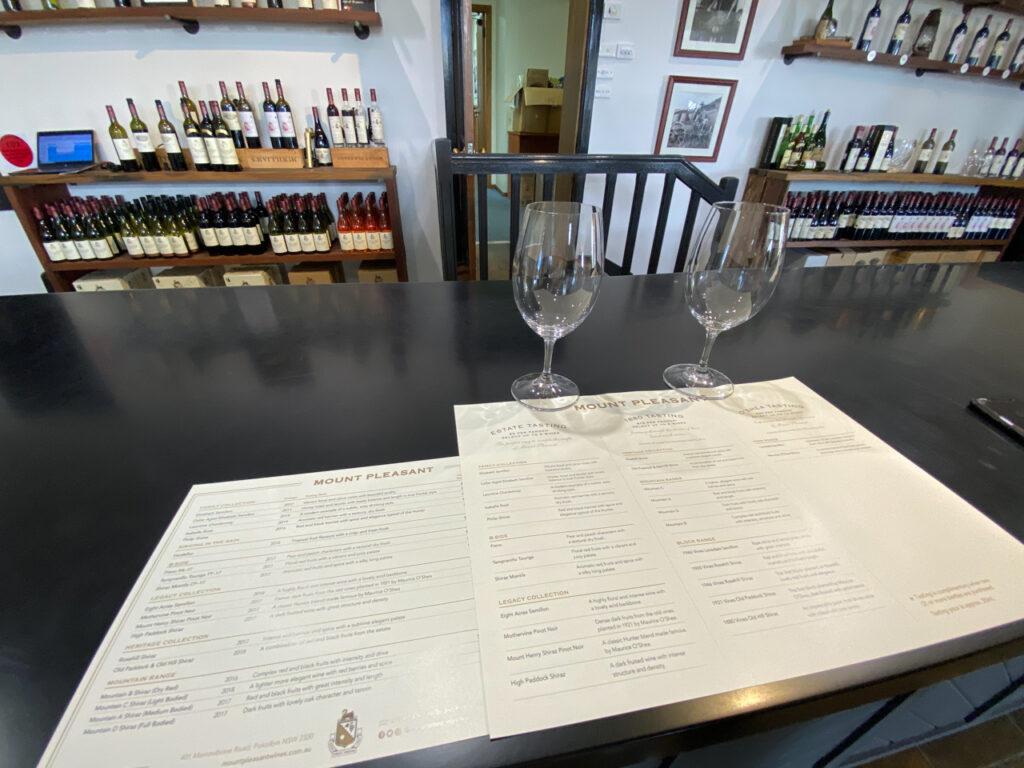 Two wine glasses on a table with wine bottles in the background.