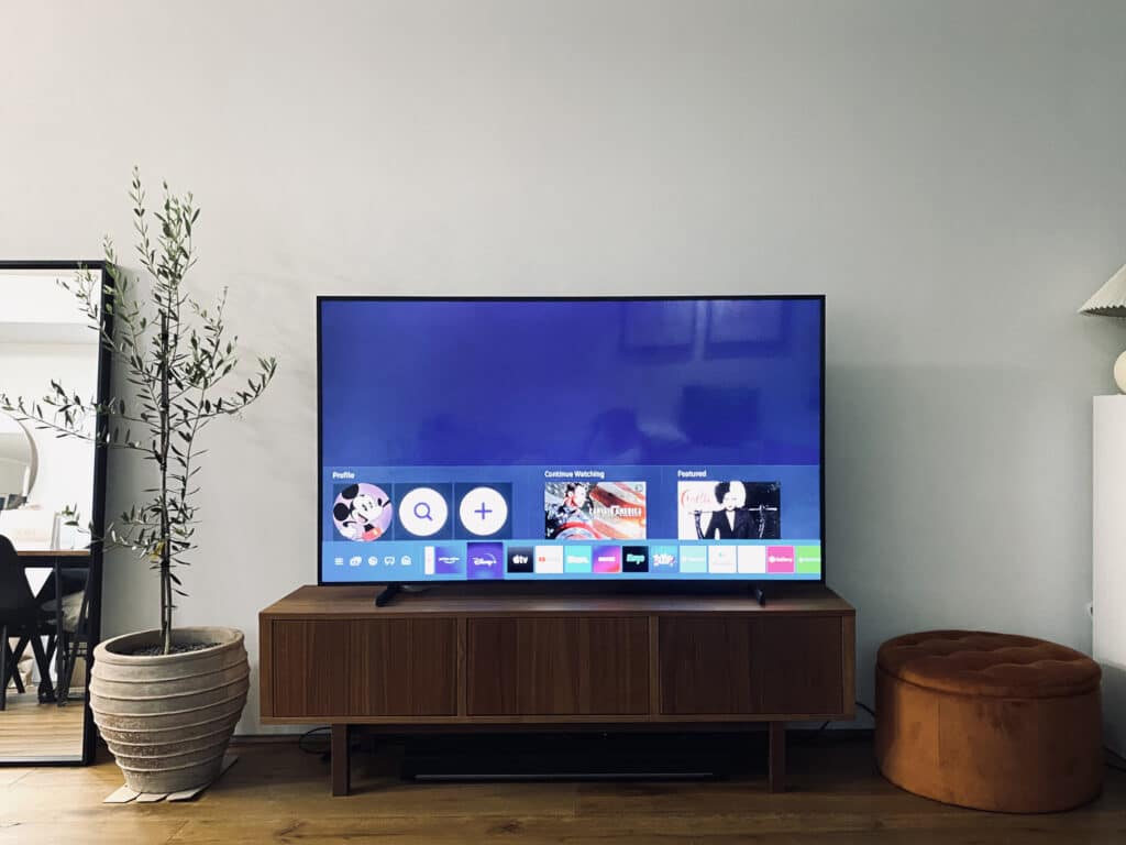 65-inch Samsung Frame TV 2021 model on a brown wood entertainment unit displaying the Home Screen